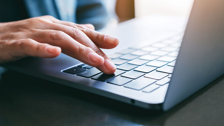 This is an image of someone operating a laptop with just a hand visible on the keyboard