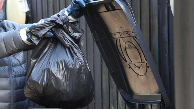 This in an image of a person putting a bag of rubbish into a bin