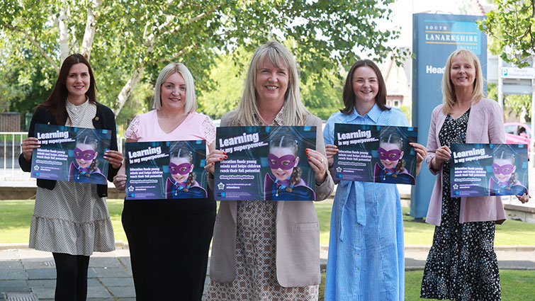 Head of Service Jacqueline Wallace is standing in the middle of a group of five female staff from Education, each displaying one of the new campaign posters.