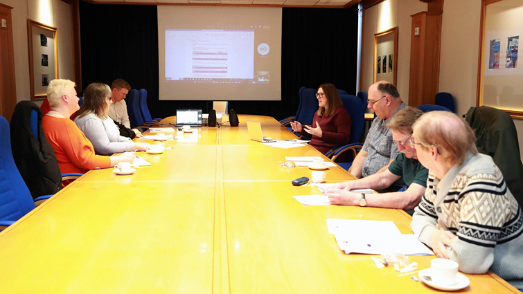This image shows members of the customer scrutiny forum at a desk with a presentation on the screen