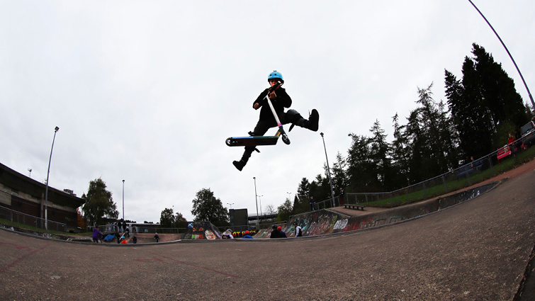 This image shows a scooter user in the air doing a trick at the new EK skatepark