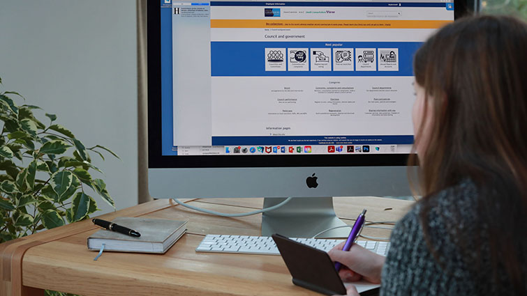 This image shows someone working at a desk taking notes while looking at a computer screen