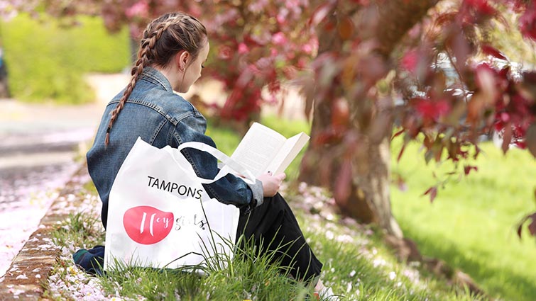 young female reading a book with a bag advertising tampons next to her