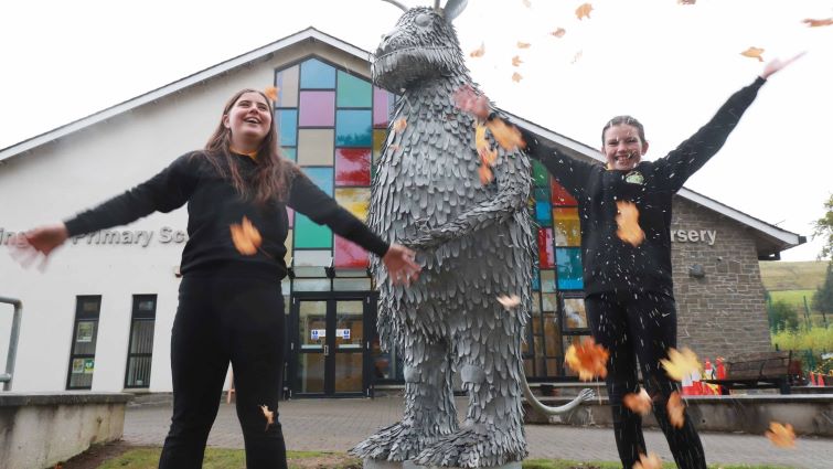 Two senior girls from Abington ps, throw leaves in the air as they stand next to the newly unveiled Gruffalo statue in front of Abington primary school.