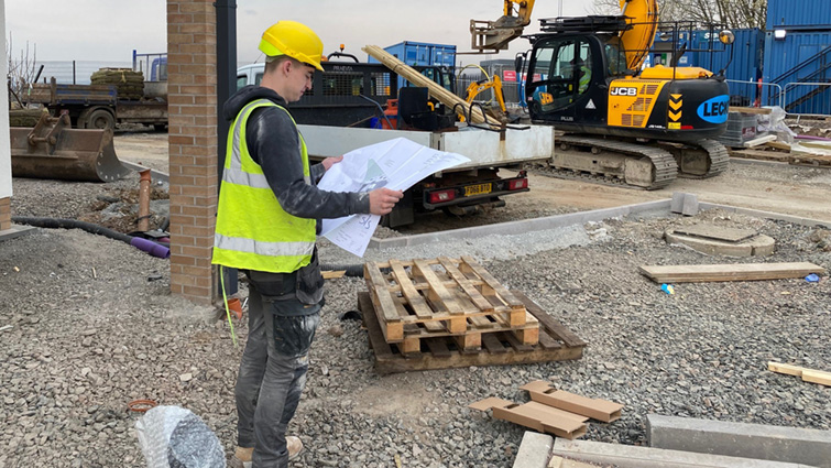 A Building Standards Modern Apprentice consults plans on a building site.