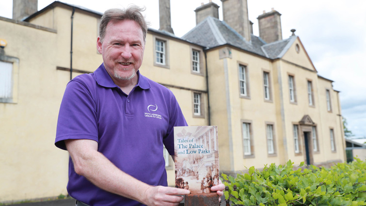 This image shows SLLC employee Peter Kerr with the Tales of the Palace and Low Parks booklet outside Low Parks Museum