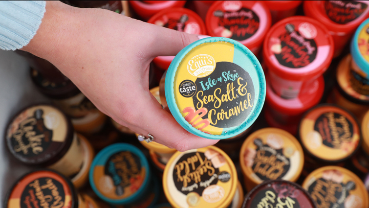 A hand picking a tub of Equi's ice cream from a display freezer full of different flavours.