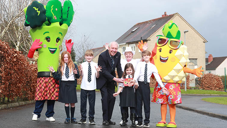 This image shows Councillor Robert Brown with welcomed Paula Pineapple and Becky Broccoli and pupils from Townhill Primary School as part of a drive to encourage pupils to have a school lunch