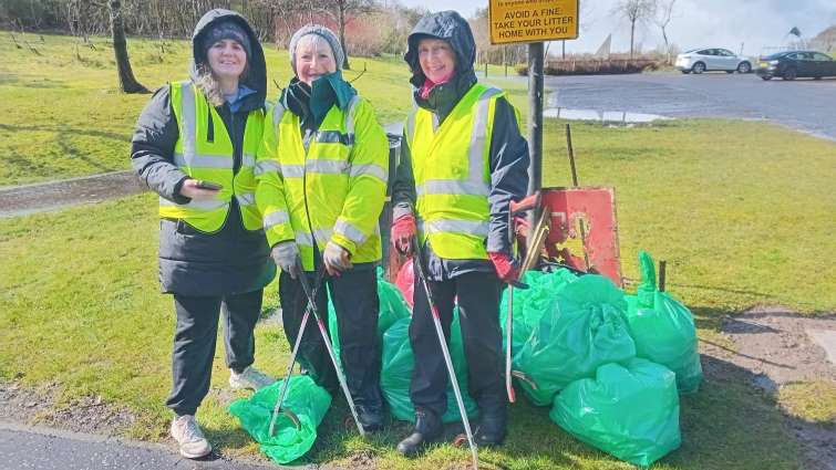 small group with full bags of waste standing next to litter warning sign