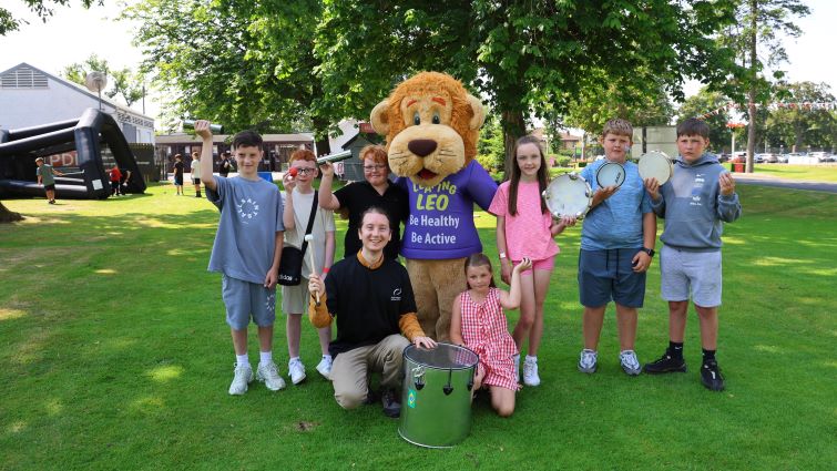 This image shows young people with mascot Leo the Lion at the SLLC Community Race Day at Hamilton Park