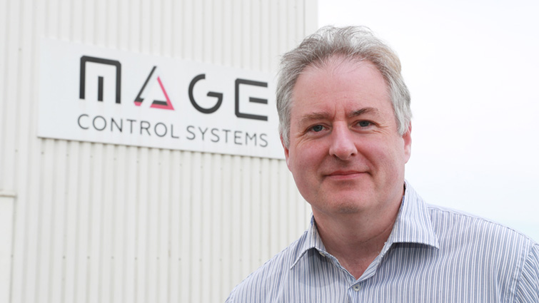 This image shows Mage Control Systems Managing Director Matthew Love in front of a sign for the company