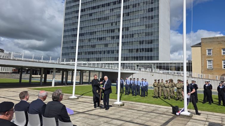This image shows Interim Provost Bert Thomson giving a speech in front of council HQ at the flag raising ceremony for Armed Forces Day 2026. Next to him is Rev Ross Blackman of Hamilton Old Parish Church, with military personnel in the background