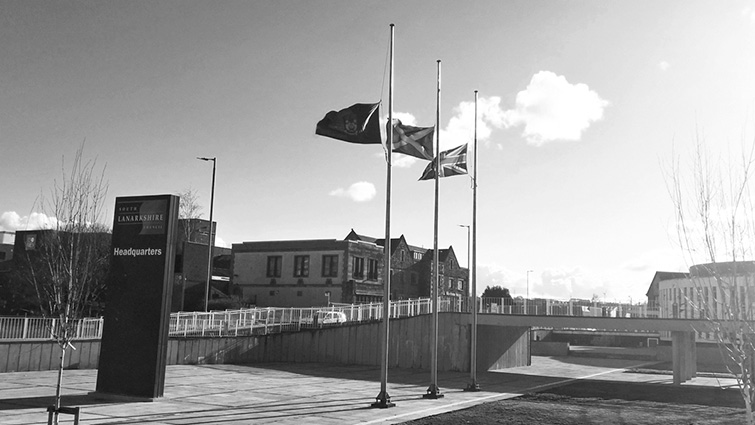 This image shows flags outside council HQ in Hamilton flying at half mast in black and white