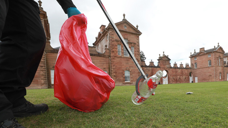 This photo shows a litter picker collecting dumped rubbish from the front lawns of Chatelherault country park