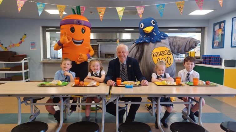 Calderwood Primary School pupils enjoying lunch with Chair of Community and Enterprise Resources Committee Councillor Robert Brown (chair of Rutherglen 900) and special guests Go Fresh Club's Colin the Carrot and Dougie the Pigeon (Rutherglen 900 mascot)