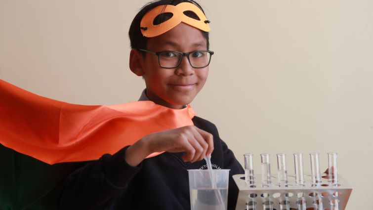In this image P7 pupil Darius is mixing a science experiment while dressed in an orange superhero cape and mask.